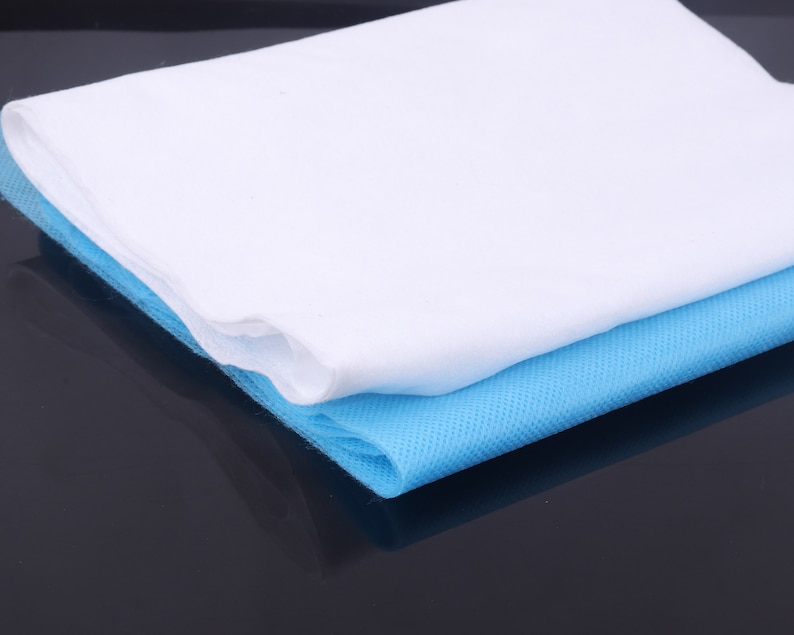 May include: A white and light blue non-woven fabric sheet. The sheet is folded in half and the white side is on top. The sheet is made of a soft, breathable material.