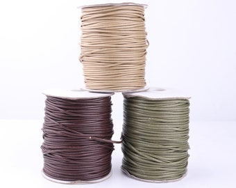May include: Three spools of waxed cord in brown, beige, and green. The cord is wound around white cardboard spools.