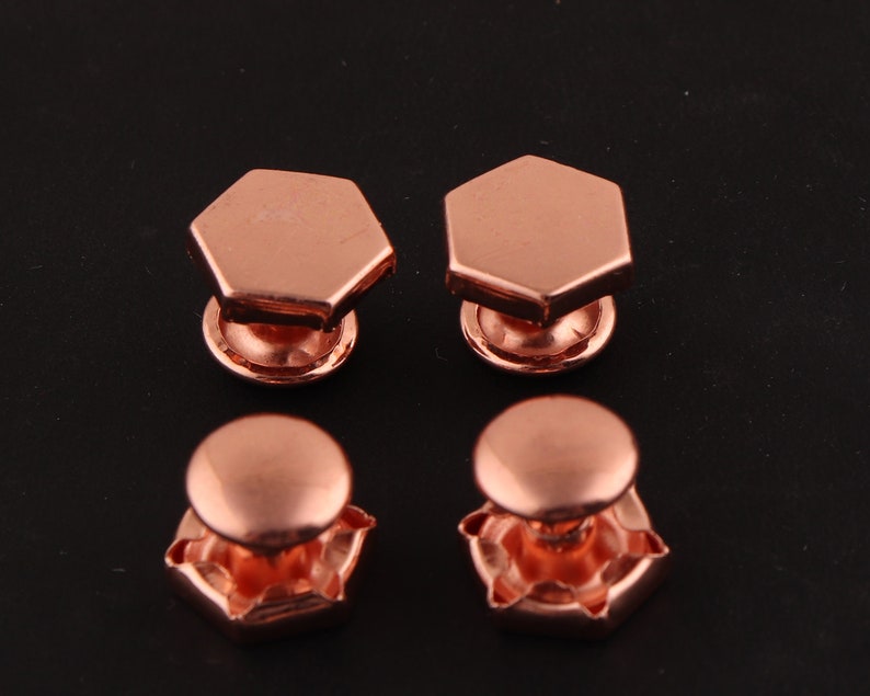 May include: Four copper-colored cufflinks. Two cufflinks have a hexagonal shape with a rounded top. The other two cufflinks have a rounded top with a hexagonal base.