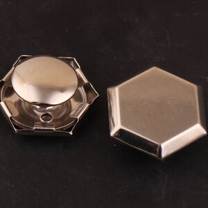 May include: Two silver metal hexagonal shaped buttons. One button has a raised dome in the center.