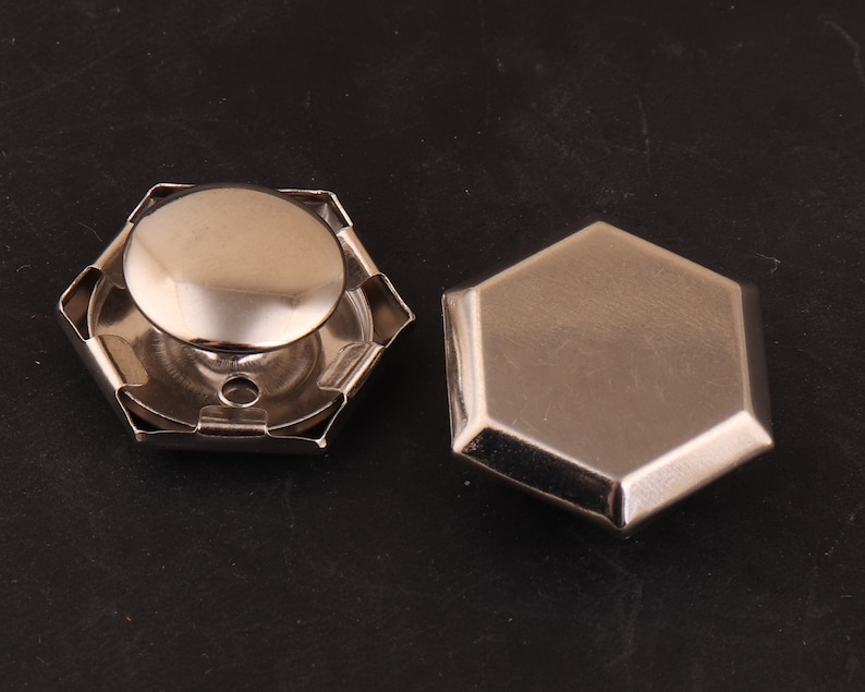 May include: Two silver metal hexagonal shaped buttons. One button has a raised dome in the center.