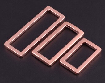May include: Three rose gold metal rectangular rings of different sizes. The rings are smooth and have a polished finish.