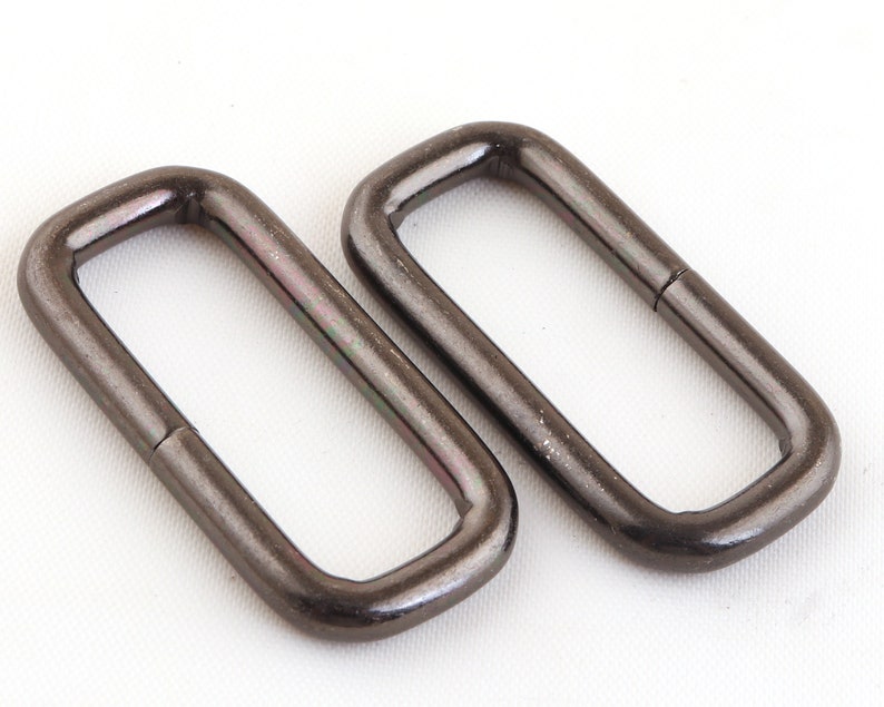 May include: Two black metal D-rings, each with a smooth, rounded edge. The rings are approximately 2.5 cm in diameter.
