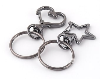 May include: Two black metal keychains with a heart and star design. One keychain has a heart-shaped loop and a round ring. The other keychain has a star-shaped loop and a round ring.