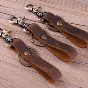 May include: Three leather keychains with antique brass key rings and clasps. The keychains are brown and have a distressed look.
