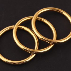 May include: Three gold-colored metal bangles stacked on top of each other.