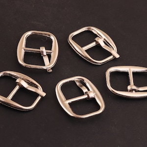 May include: Five silver-toned metal belt buckle closures. The buckles are rectangular with a smooth finish and a rounded edge.
