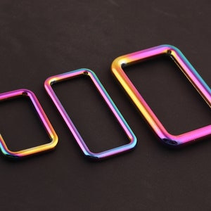 Może przedstawiać: Trzy tęczowe metalowe pierścienie w r&oacute;żnych rozmiarach. Pierścienie są prostokątne i mają gładkie, polerowane wykończenie.