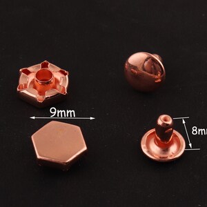 May include: Two rose gold metal rivets, one with a 9 mm diameter and the other with an 8 mm diameter. The rivets have a domed top and a flat base.