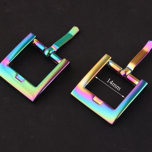 Może przedstawiać: Dwa iryzujące metalowe zapięcia do paska. Klamra po prawej stronie ma wymiar 14 mm.