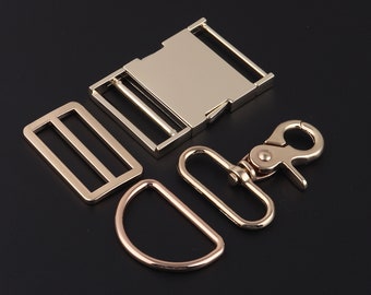 May include: A set of four gold-toned metal hardware pieces for crafting. The set includes a buckle, a slider, a D-ring, and a hook.