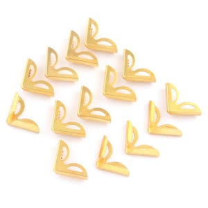 May include: A collection of gold-colored, right-angle corner brackets. Each bracket has a decorative cutout design. The brackets are arranged on a white background, suggesting their use in crafts or decorative projects.
