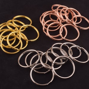May include: A collection of key rings in gold, rose gold, and silver. The key rings are all the same size and shape, and they are arranged in a pile.