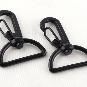 Puede incluir: Dos ganchos giratorios de metal negro con un anillo en D. Los ganchos están cerrados y listos para ser unidos a una bolsa, llavero u otro artículo.