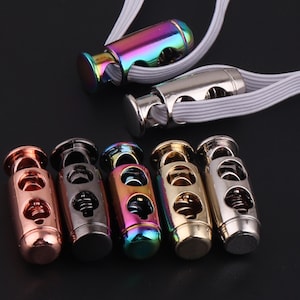 May include: Six metal cord stoppers in different colours, including gold, silver, black, and rainbow. The stoppers have a spring mechanism to hold cords in place.