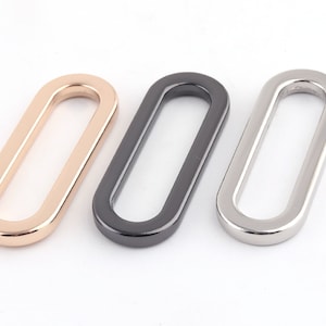 May include: Three oval-shaped metal rings in gold, black, and silver.