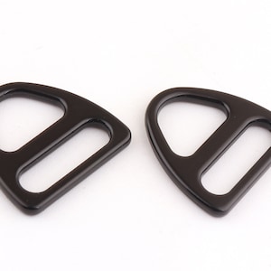 Op de afbeelding: Twee zwarte metalen D-ring gespen met een driehoekige vorm. De gespen hebben een gladde, glanzende afwerking.