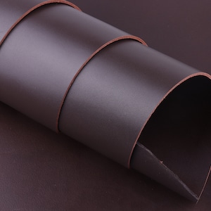May include: Close-up of a roll of dark brown leather. The leather is smooth and has a slight sheen.