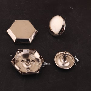 May include: Four silver metal rivets, two with a hexagonal base, one with a round base, and one with a round base and a post. The hexagonal rivets measure 21 mm in diameter, the round rivets measure 10 mm in diameter.