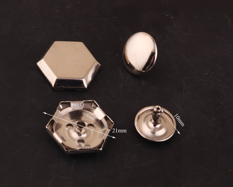 May include: Four silver metal rivets, two with a hexagonal base, one with a round base, and one with a round base and a post. The hexagonal rivets measure 21 mm in diameter, the round rivets measure 10 mm in diameter.