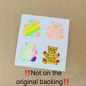 May include: Four bear-shaped stickers on a white square sheet. The top left bear has rainbow stripes, the top right has pink hearts, the bottom left has a holographic dot pattern, and the bottom right has colorful geometric shapes. Text reads: !!Not on the original backing!!