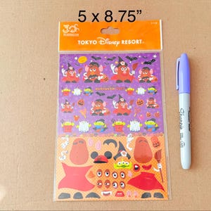 May include: A Tokyo Disney Resort Halloween 2013 sticker sheet measuring 5 x 8.75 inches. The sheet features purple and orange backgrounds with Mr. Potato Head characters in costumes, ghosts, and aliens. A light purple Sharpie marker is placed beside it.