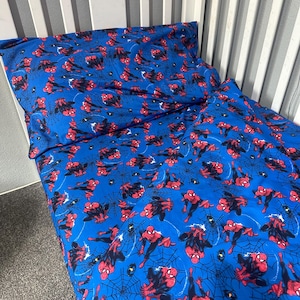 May include: A blue bed sheet set featuring a repeating pattern of Spider-Man in red and blue suits, interspersed with black spider web graphics. The set includes a pillowcase and a fitted sheet, both displaying the same character print.