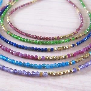 May include: A set of seven necklaces with different colored gemstone beads. The necklaces are layered on top of each other, with the amethyst beads at the bottom and the gold beads at the top.