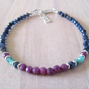 Op de afbeelding: Een kralenarmband met gefacetteerde donkerblauwe saffierkleurige kralen, levendige magentaroze kralen en kleine lichtgroene kralen. Het ontwerp bevat zilverkleurige metalen tussenstukjes en een zilverkleurige karabijnsluiting met een verstelketting.