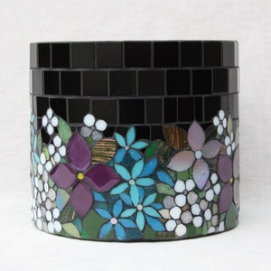 May include: A black mosaic planter with a floral design around the top. The flowers are purple, blue, and white.
