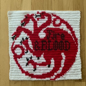 Puede incluir: Cuadrado blanco de crochet con un dragón rojo de tres cabezas y las palabras "Fire & Blood" en negro.