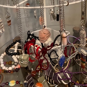May include: A variety of crystal necklaces and bracelets on display. The necklaces feature different types of crystals, including rose quartz, amethyst, and lapis lazuli. The bracelets are made with various beads, including black onyx, white agate, and tiger's eye.