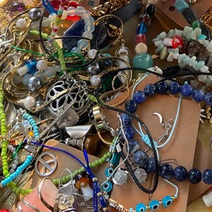 Może przedstawiać: Kolekcja r&oacute;żnych element&oacute;w biżuterii, w tym naszyjniki, bransoletki i kolczyki. Biżuteria zawiera mieszankę materiał&oacute;w, takich jak koraliki, metal i kamienie szlachetne, w r&oacute;żnych kolorach, w tym złotym, srebrnym, niebieskim i zielonym. Niekt&oacute;re elementy mają zawieszki.