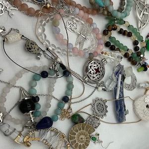 May include: A collection of jewelry featuring various charms, beads, and pendants. The jewelry includes a variety of colors and materials, such as silver, gold, and gemstones. The charms include a dragonfly, a star, a crescent moon, and a heart. The beads include amethyst, agate, and turquoise. The pendants include a crystal, a locket, and a charm with the text "Always have a smile in your heart".