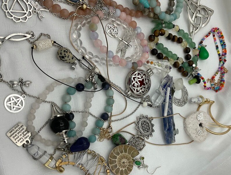 May include: A collection of jewelry featuring various charms, beads, and pendants. The jewelry includes a variety of colors and materials, such as silver, gold, and gemstones. The charms include a dragonfly, a star, a crescent moon, and a heart. The beads include amethyst, agate, and turquoise. The pendants include a crystal, a locket, and a charm with the text "Always have a smile in your heart".