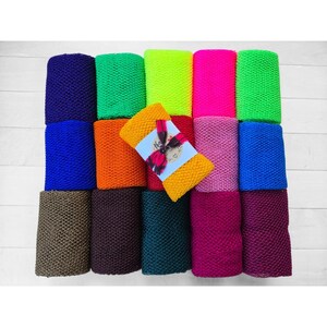May include: A set of 12 colorful bath poufs, arranged in a rectangle. The poufs are made of a mesh material and come in a variety of colors, including green, blue, purple, orange, and yellow. One pouf is wrapped in a plaid gift wrap with a tag that says "The Knot".