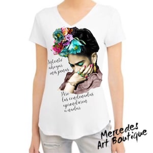 Op de afbeelding: Witte V-hals T-shirt met een portret van een vrouw met bloemen en sieraden. Het ontwerp bevat de Spaanse tekst "Intenté ahogar mis penas... Pero las condenadas aprendieron a nadar" en de winkelnaam "Mercedes Art Boutique".