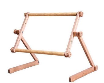 May include: A wooden embroidery hoop stand with adjustable legs. The stand is made of natural wood and has a light brown finish. The hoop is made of wood and has a natural finish.