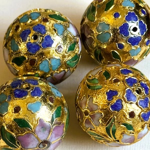 May include: Three spherical beads featuring a gold-tone textured surface decorated with colorful enamel floral patterns in shades of blue, green, pink, and white. Each bead has a small central hole, showcasing intricate metalwork and vibrant enamel.