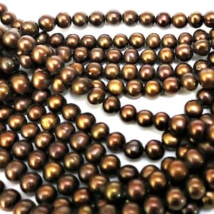 May include: A strand of brown freshwater pearls. The pearls are round and have a slight iridescent sheen.
