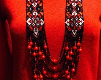 May include: A long, multi-strand beaded necklace with red and black beads. The necklace features a central section of intricate beadwork in red, white, and black.