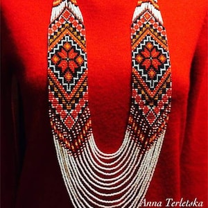 May include: A long, multi-strand necklace made of white and red beads with a geometric pattern. The necklace is worn on a red sweater. The text "Anna Terletska" is visible at the bottom of the image.