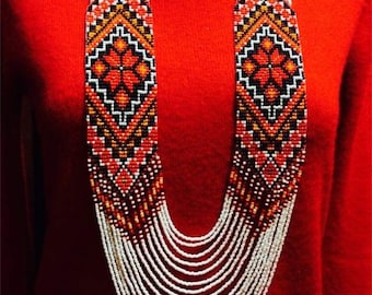 May include: A long, multi-strand necklace made of white and red beads with a geometric pattern. The necklace is worn on a red sweater. The text "Anna Terletska" is visible at the bottom of the image.