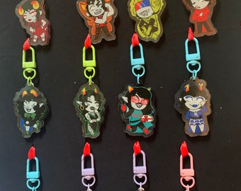 May include: Twelve colorful keychains featuring cartoon characters with different expressions and poses. Each keychain has a metal clasp and a clear background.
