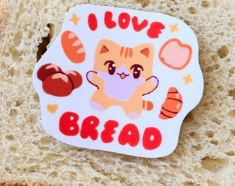 May include: A white sticker with a cartoon orange cat with pink cheeks and a pink nose. The cat is surrounded by bread-shaped objects and the text "I LOVE BREAD" in red letters.