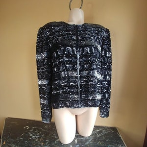 May include: A black and silver sequined jacket with a zipper closure. The jacket has a geometric pattern and is on a mannequin.