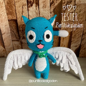 May include: A handmade blue crochet cat doll with white wings, a green scarf, and a pink tongue. The doll has large white eyes with black pupils and the text "TESTER Puntitodealgodon".