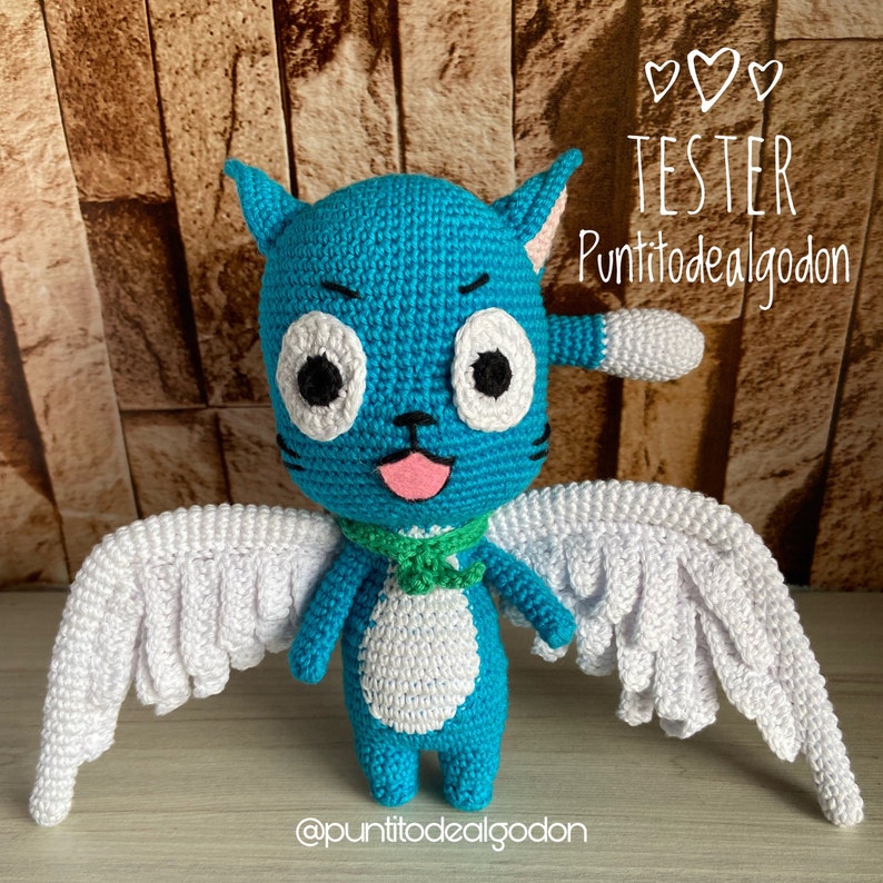 May include: A handmade blue crochet cat doll with white wings, a green scarf, and a pink tongue. The doll has large white eyes with black pupils and the text "TESTER Puntitodealgodon".