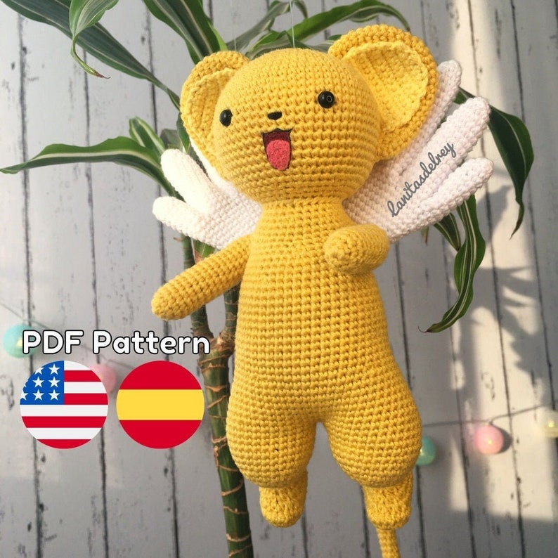 Puede incluir: Un juguete de peluche amarillo tejido a crochet con alas blancas. El juguete tiene una cara de dibujos animados con ojos negros, una lengua rosa que sobresale y una sonrisa blanca. El juguete est&aacute; etiquetado con "lainitasdelrey" en el ala. El texto "PDF Pattern" est&aacute; debajo del juguete, con una bandera estadounidense y una bandera espa&ntilde;ola a cada lado.