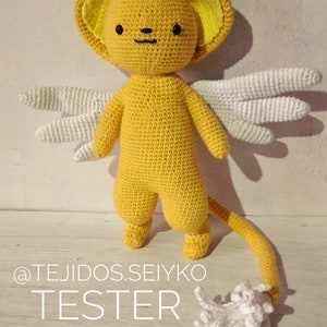 Puede incluir: Un juguete de peluche amarillo tejido a crochet con alas blancas y cola. El juguete tiene una cabeza redonda con ojos negros y una nariz negra. El juguete est&aacute; de pie sobre una superficie de madera. El texto "@TEJIDOS.SEIYKO TESTER" es visible en la imagen.
